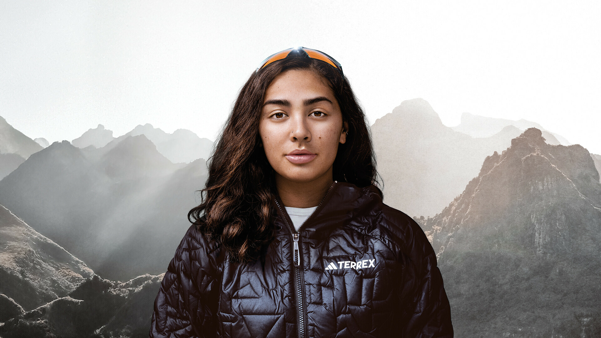 Portrait of Samantha Soriano looking directly at the camera. She is wearing a black outdoor jacket and has sunglasses on her head. Misty mountain peaks are visible in the background.